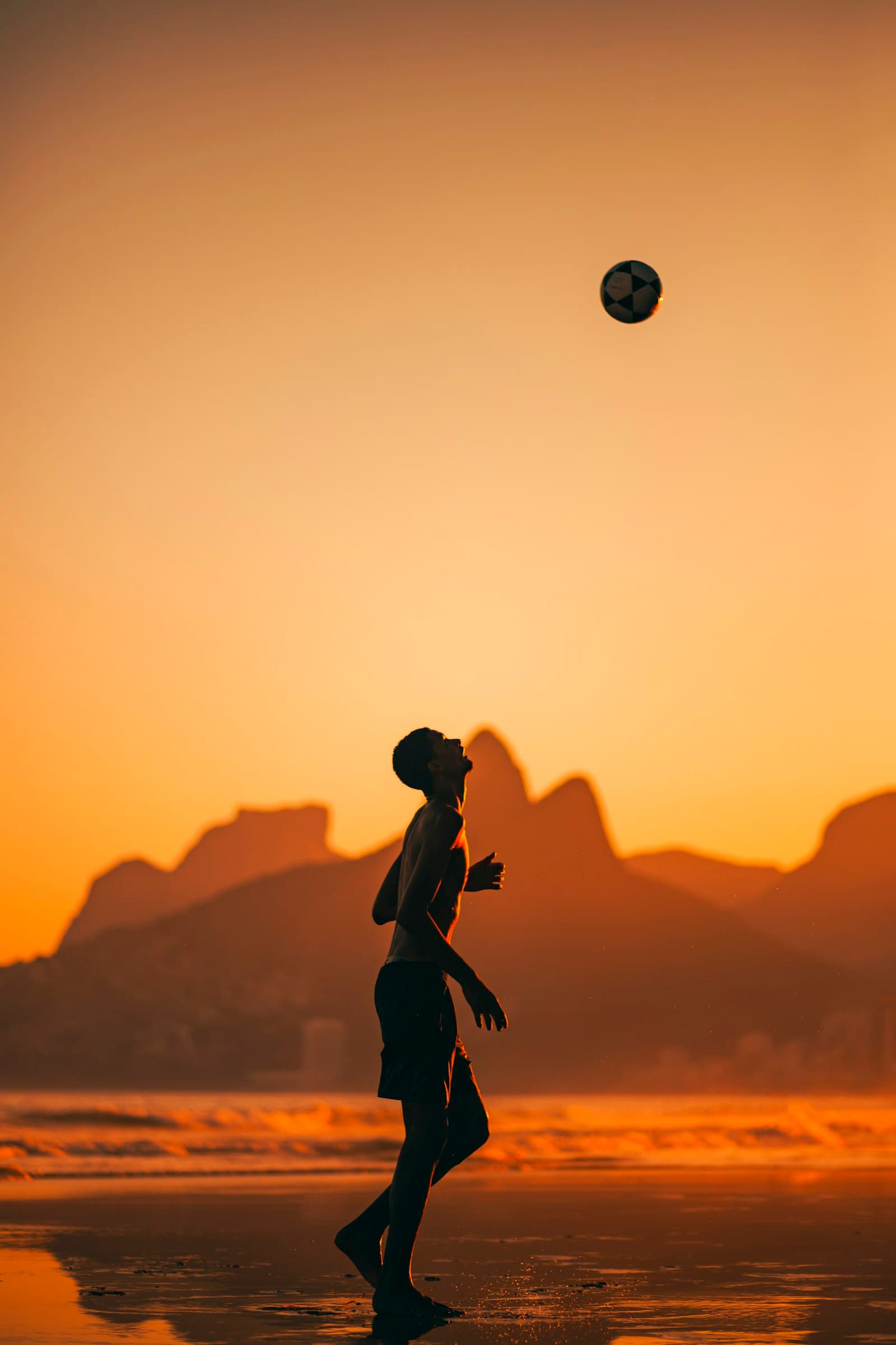 A player juggling a ball on the beach at sunset in Rio de Janeiro