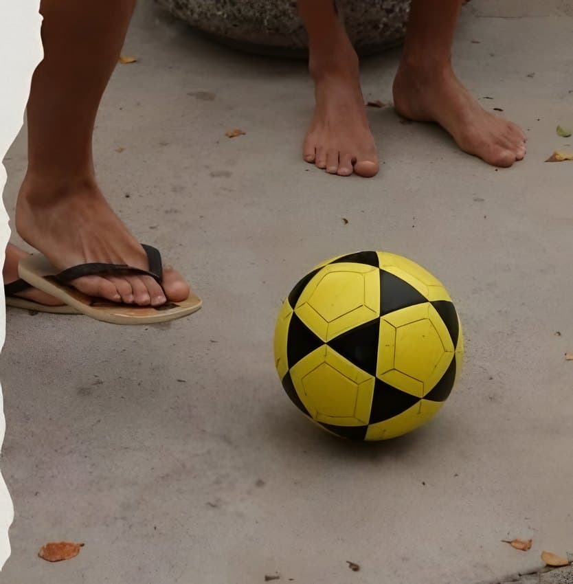 Bare feet and flip-flops next to a yellow and black footvolley ball